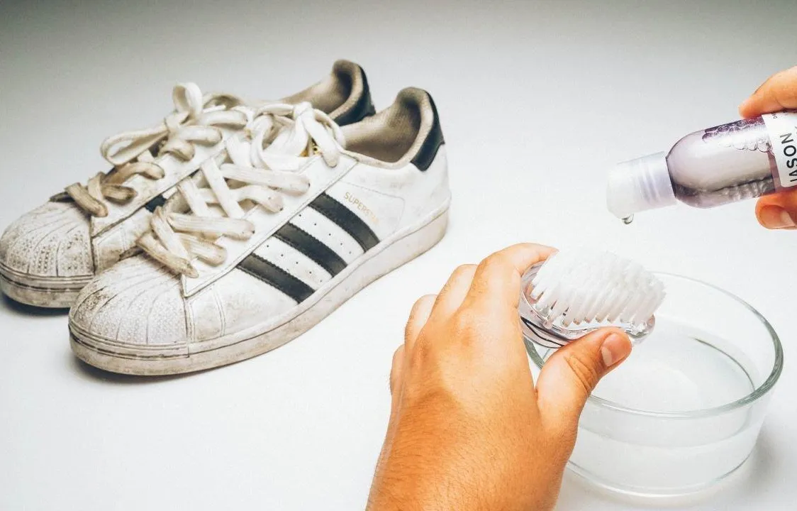 White sneakers being cleaned with a brush and cleaning solution