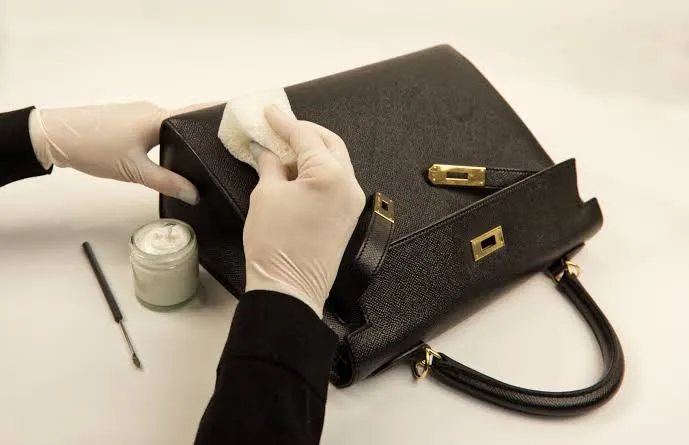 Gloved hands cleaning a black structured leather handbag
