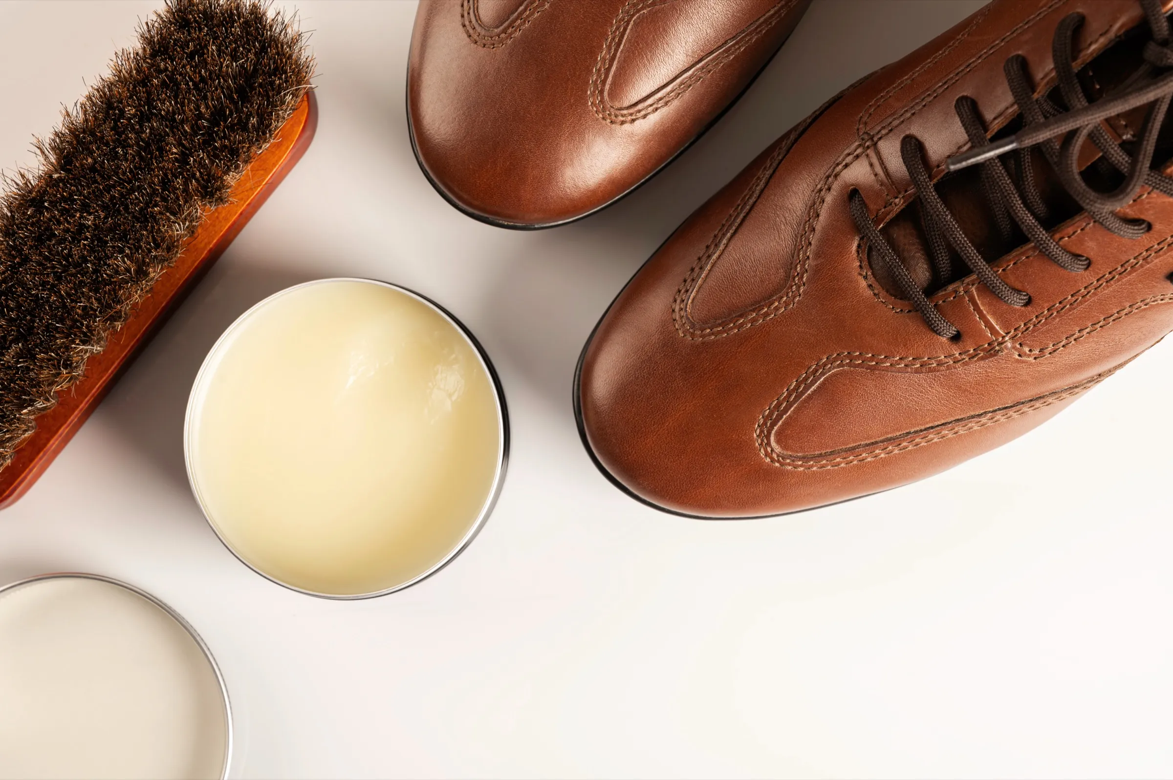 Brown leather shoes beside a horsehair brush and leather conditioner